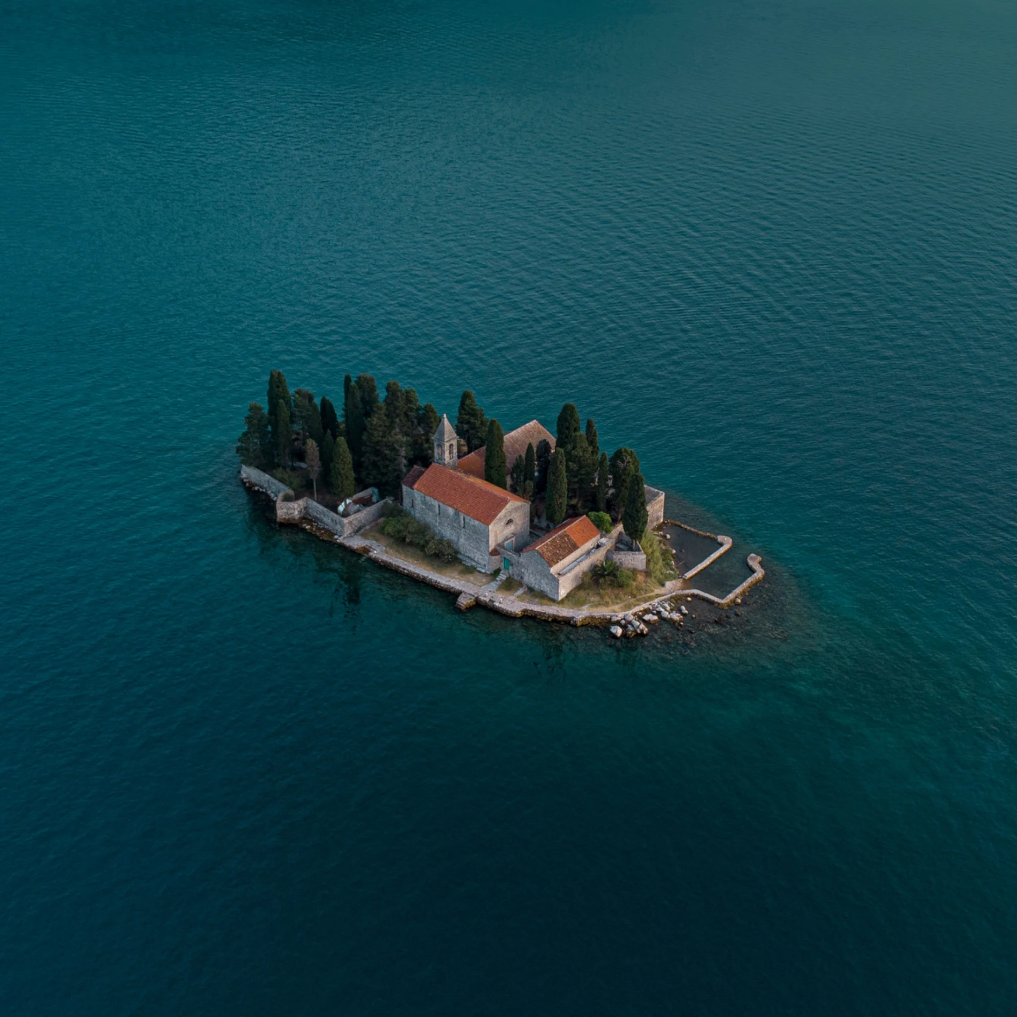 Petit îlot avec bâtiments en pierre et cyprès dans une eau turquoise